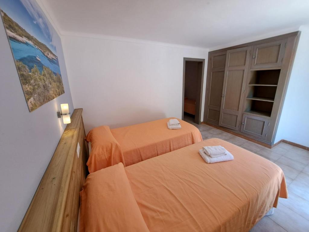 two beds in a room with orange sheets at Hostal Playa in Cala Santanyi