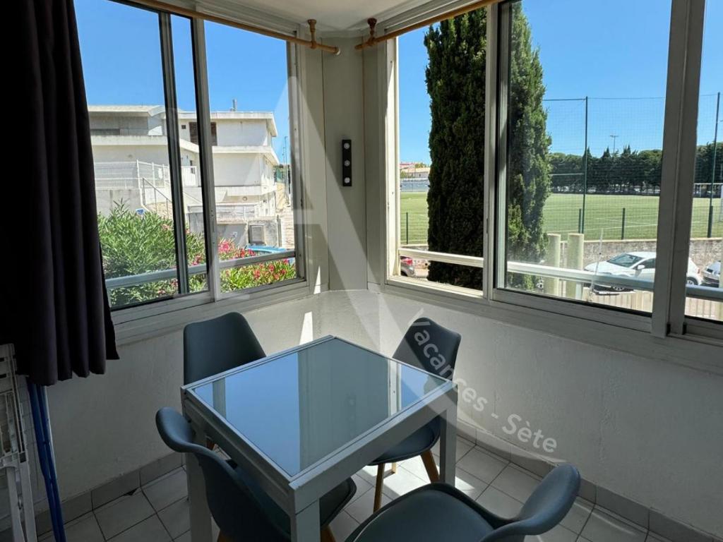 une table en verre et deux chaises dans une pièce avec fenêtres dans l'établissement LA PLAGE AU BOUT DE LA RUE, à Sète