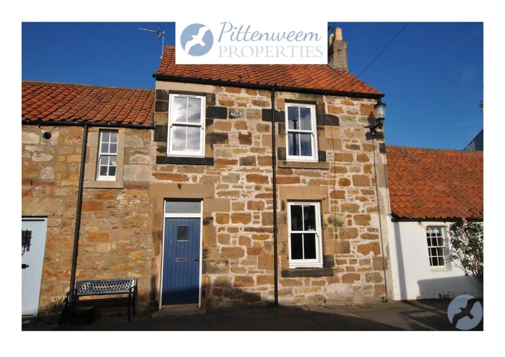 un edificio de ladrillo con una puerta azul y un cartel en él en Willow Cottage- charming cottage in East Neuk, en Pittenweem