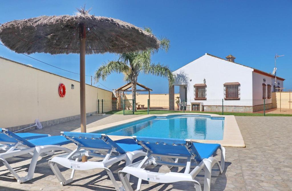 grupa krzeseł i parasol obok basenu w obiekcie Chalet Vigía 114 w mieście Conil de la Frontera