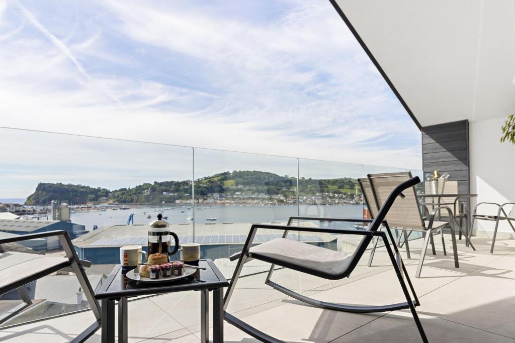 einen Balkon mit Stühlen und Tischen sowie Blick auf das Wasser in der Unterkunft Teign View, Grand Banks in Teignmouth