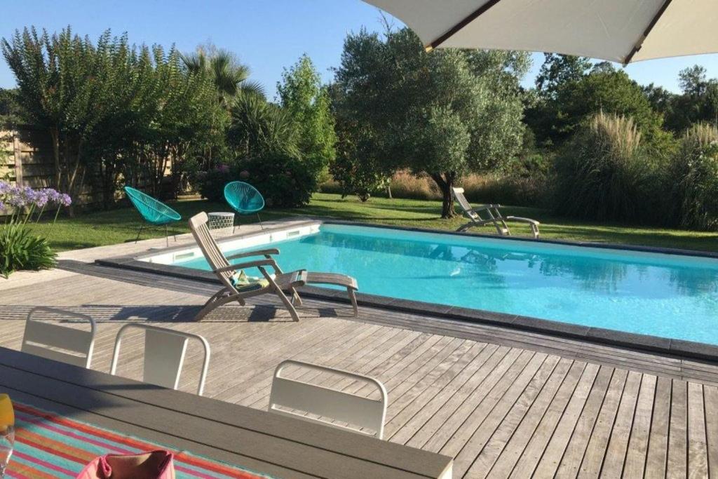 a swimming pool with chairs and an umbrella at Villa 145 m near ocean with pool and garden in Moliets-et-Maa