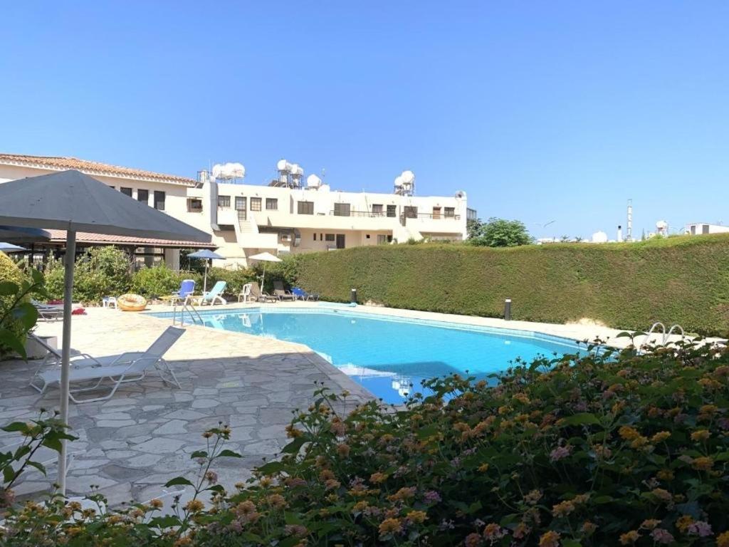 ein Schwimmbad mit Sonnenschirm und ein Gebäude in der Unterkunft Bysantium Gardens in Paphos City