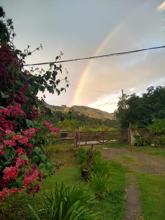 a rainbow in the sky over a yard with flowers at Mantiqueira lar doce lar in Gonçalves