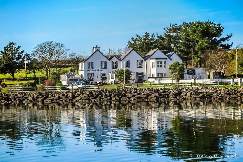 ein großes weißes Haus mit einer Steinmauer neben dem Wasser in der Unterkunft Milltown House Dingle in Dingle