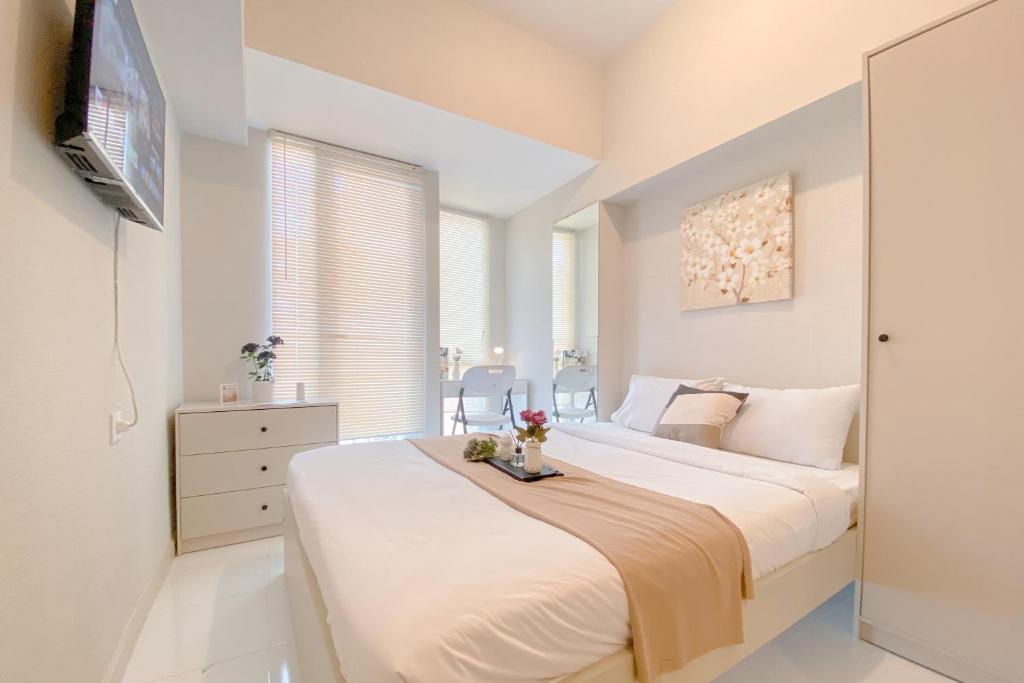 ein weißes Schlafzimmer mit einem großen Bett und einem TV in der Unterkunft Good Deal and Restful Studio at Apartment Tokyo Riverside PIK 2 By Travelio in Tangerang