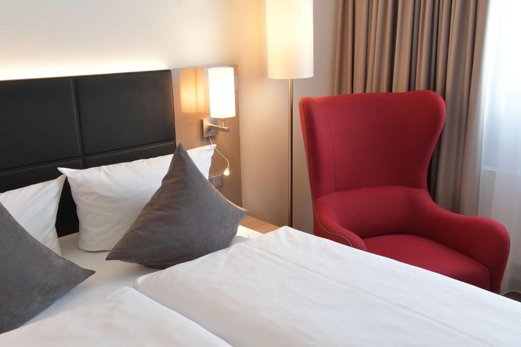 a red chair sitting next to a bed in a hotel room at Best Western Queens Hotel Pforzheim-Niefern in Pforzheim