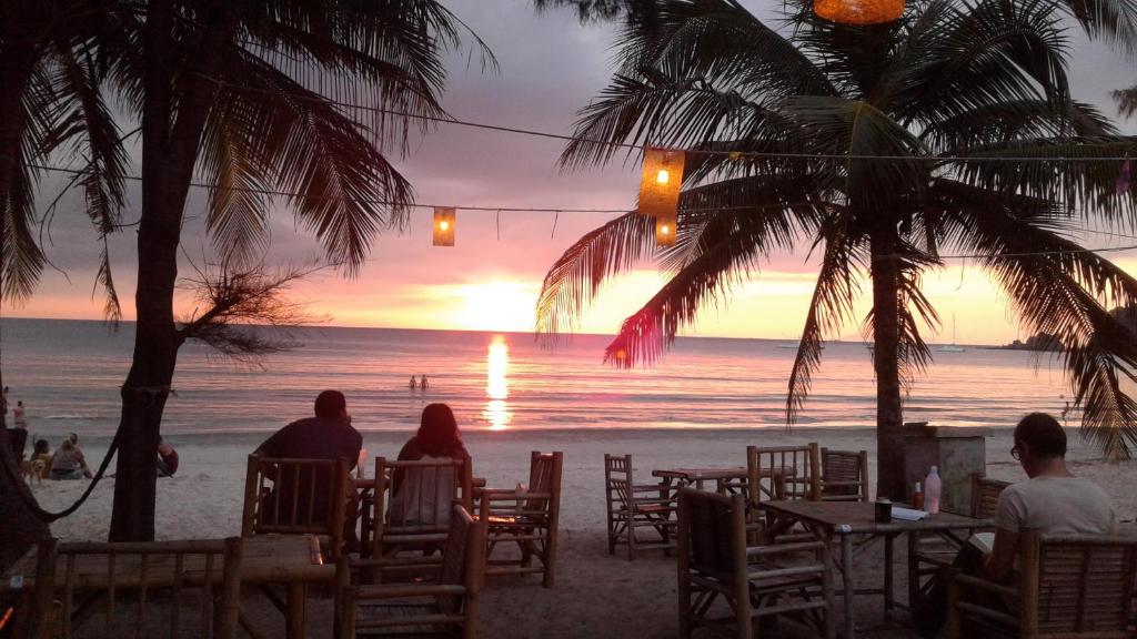 mensen die aan tafels op het strand zitten en naar de zonsondergang kijken bij Phayam Friends in Ko Phayam