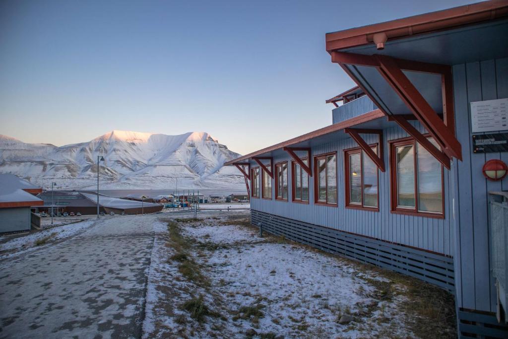 a building with snow on the ground in front of mountains at Radisson Blu Polar Hotel, Spitsbergen in Longyearbyen