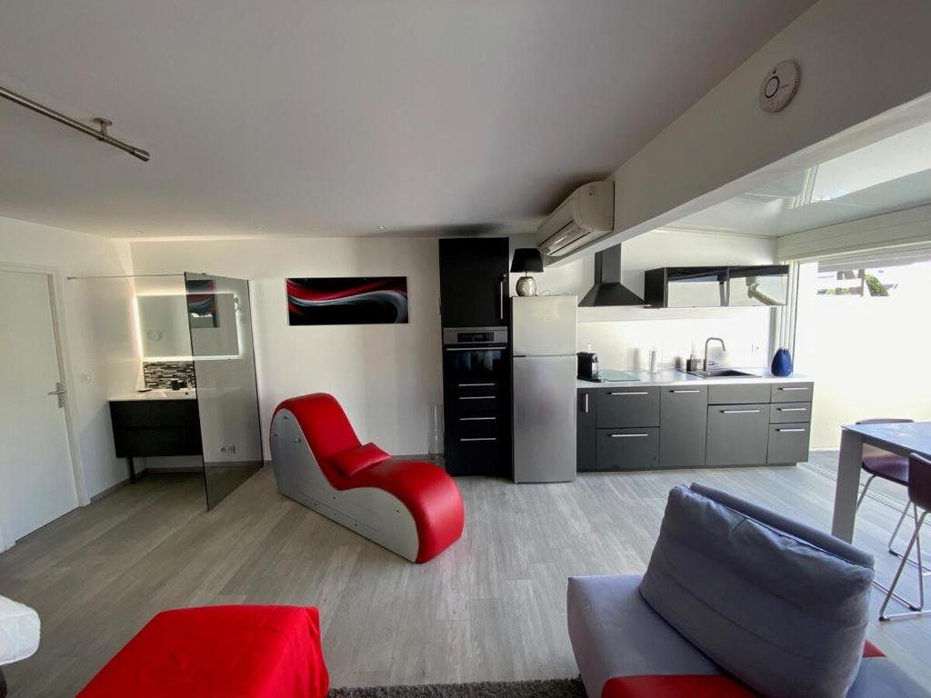 Il comprend un salon avec une chaise rouge et une cuisine. dans l'établissement Village Naturiste Villa luxe Port Nature 1, au Cap d'Agde