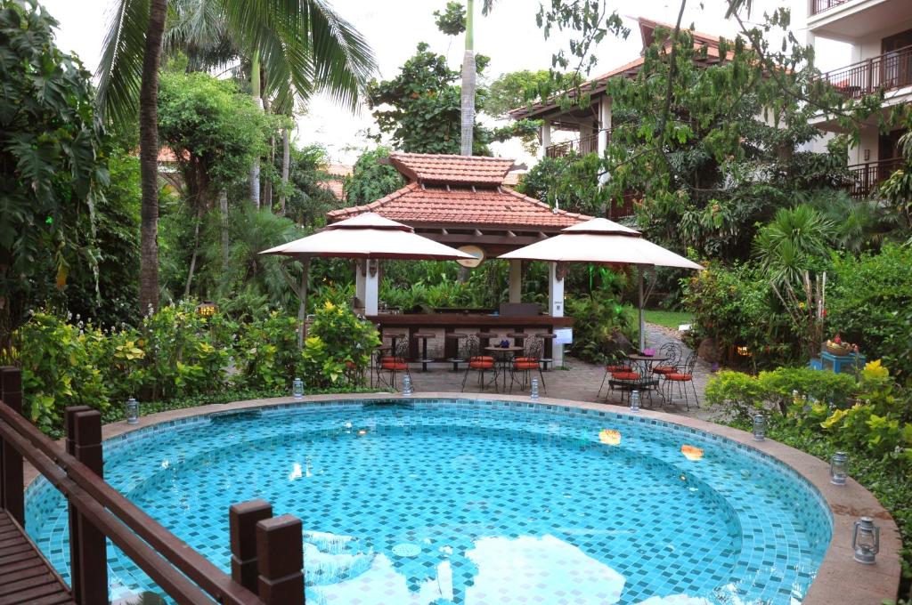 A round tiled pool sits in a lush garden beside a shaded outdoor bar or seating area.