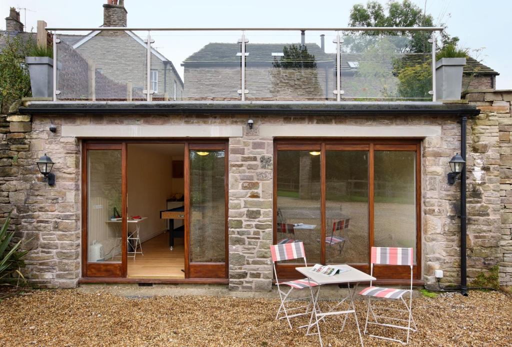 a stone house with glass doors and a table and chairs at Damson Cottage in Rainow