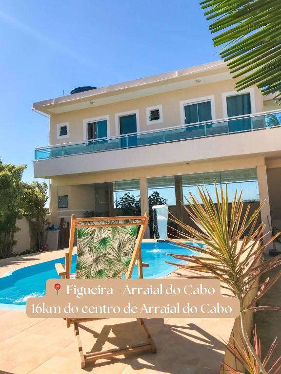 a villa with a pool and a chair in front of a house at Suítes Brandi in Arraial do Cabo