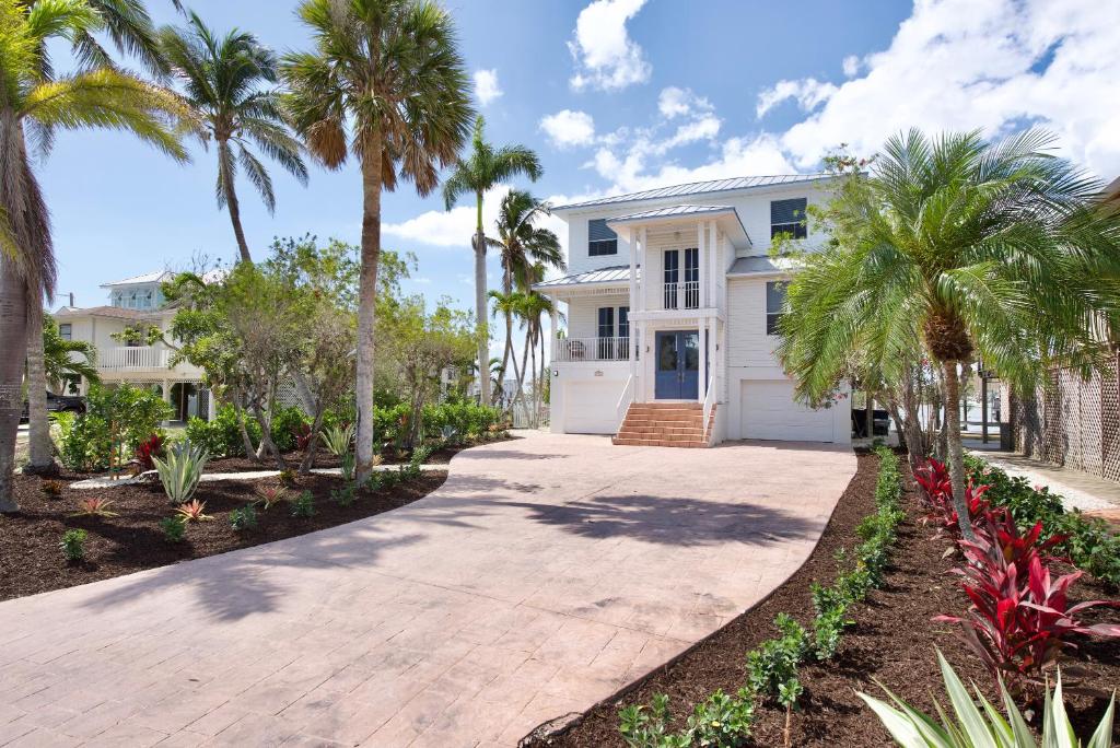 a white house with palm trees and a driveway at Dock Holiday by Sun Palace Vacations in Fort Myers Beach
