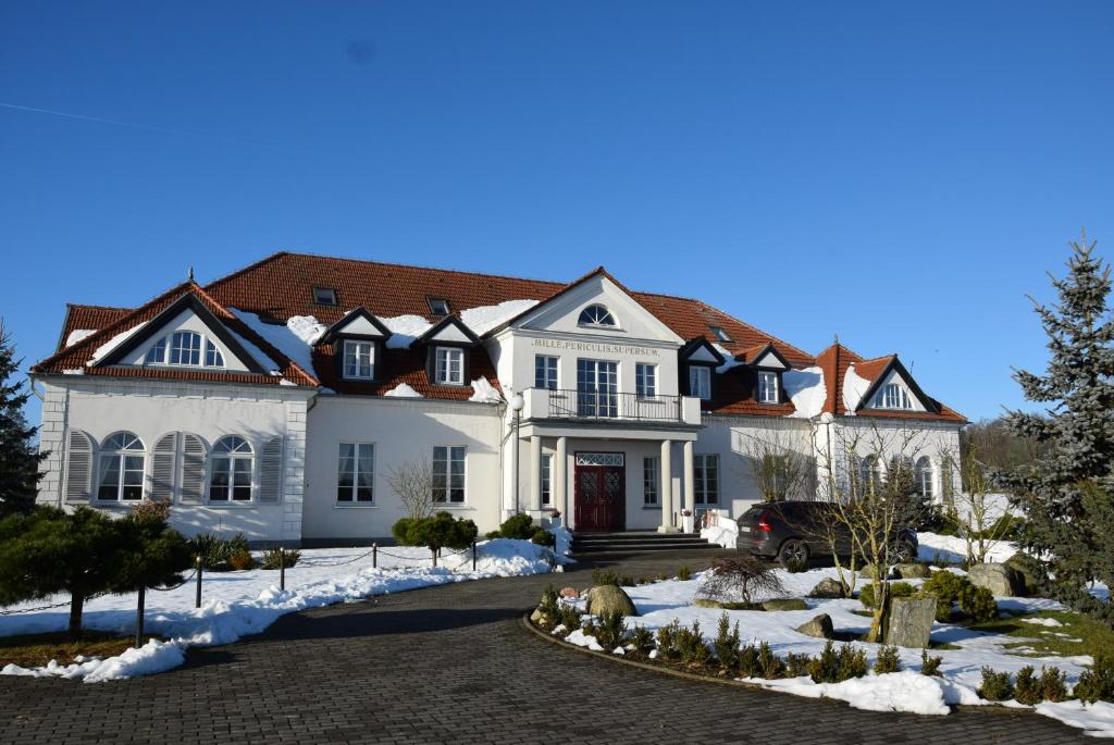Large white manor with red roof and snow-dusted grounds, paved driveway and parked car.