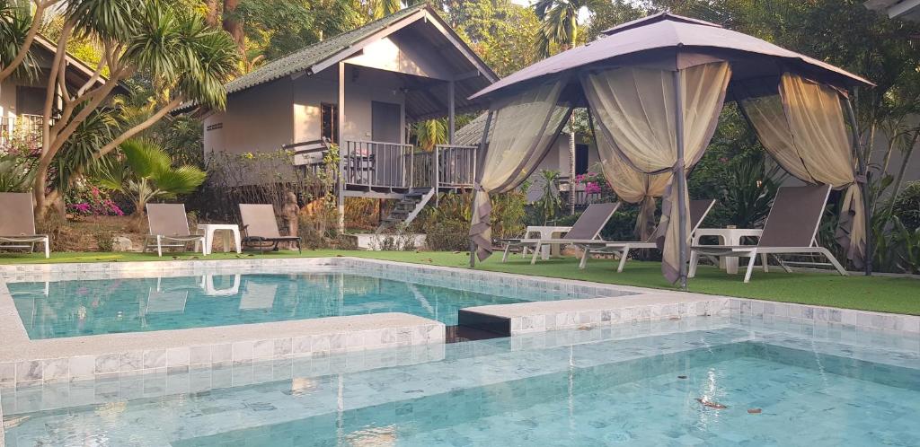 Una piscina con sillas y sombrilla y una casa. en COCOON Koh Chang, en Ko Chang