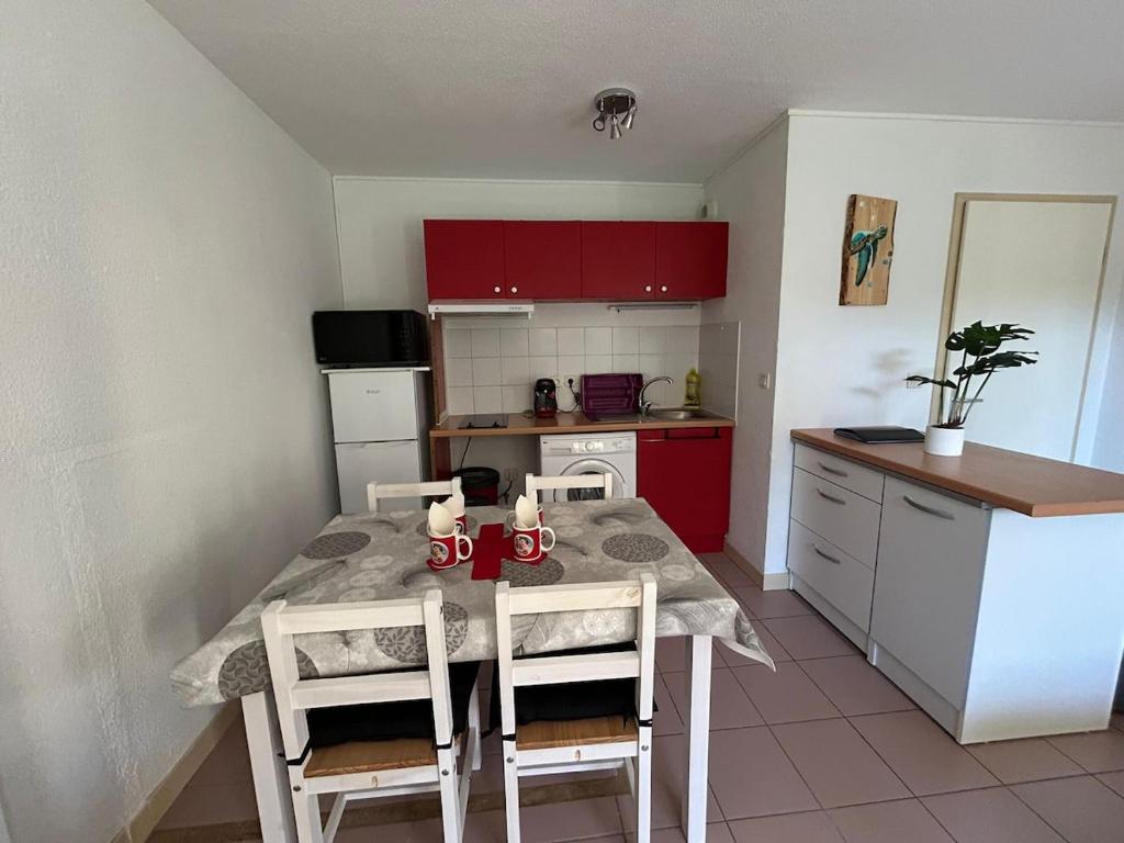 une cuisine avec une table, des chaises et des armoires rouges dans l'établissement La Belle Échappée Pyrénéenne, à Lourdes