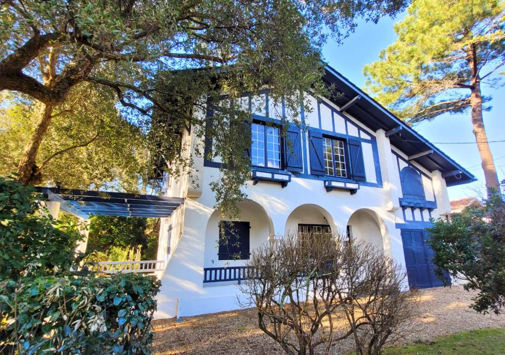 une maison blanche avec des volets bleus et des arbres dans l'établissement MAYIE THERESA - Belle villa bascolandaise entre lac et mer, à Soorts-Hossegor