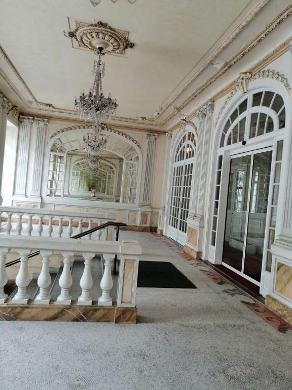 une grande pièce blanche avec un lustre et un escalier dans l'établissement Cauterets et son bel appartement, à Cauterets