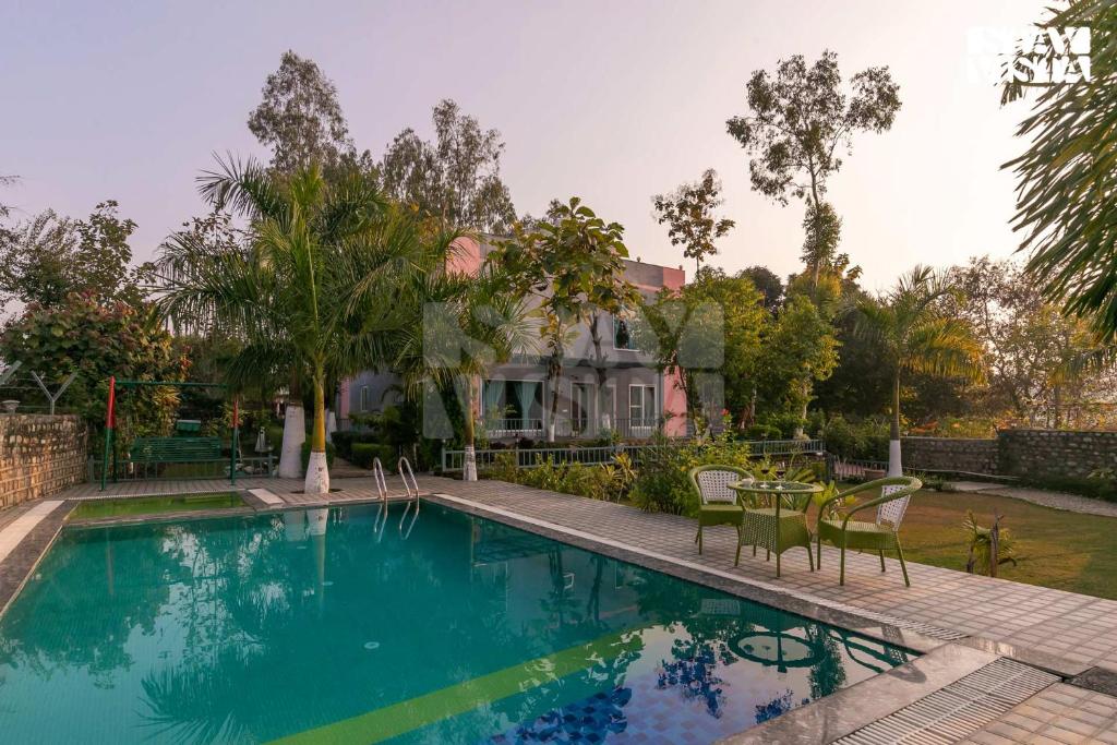 a swimming pool with chairs and a table in front of a house at Corbett Calling with Projector Set-Up by StayVista in Rāmnagar