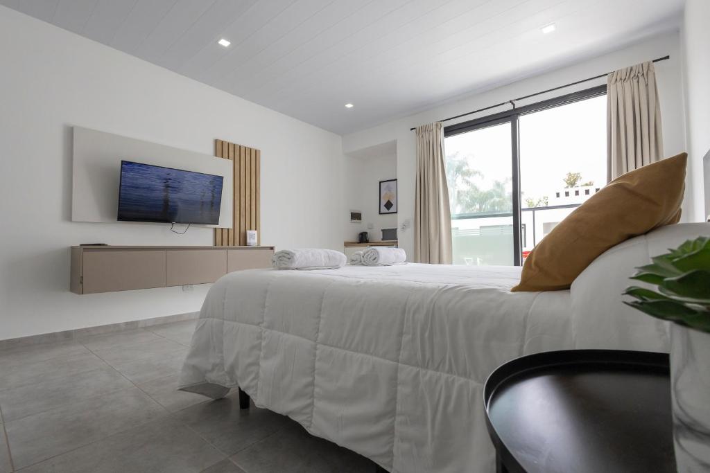 a white bedroom with a large bed and a tv at Apart Hotel & Resto Ribera del Baradero in Baradero