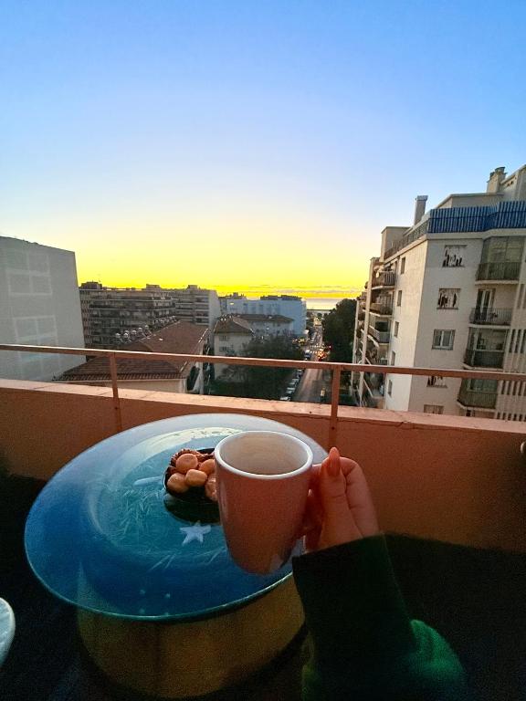 une personne tenant une tasse de café sur un balcon dans l'établissement Votre COCON Niçois, à Nice