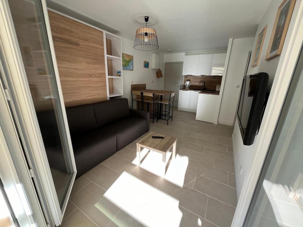 un salon avec un canapé noir et une cuisine dans l'établissement Très beau T2 4 personnes 200 m plage de la Favière, à Bormes-les-Mimosas