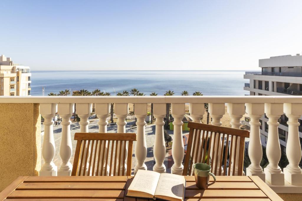 a balcony with two chairs and a table with a book at Penthouse Pink seafront in La Mata