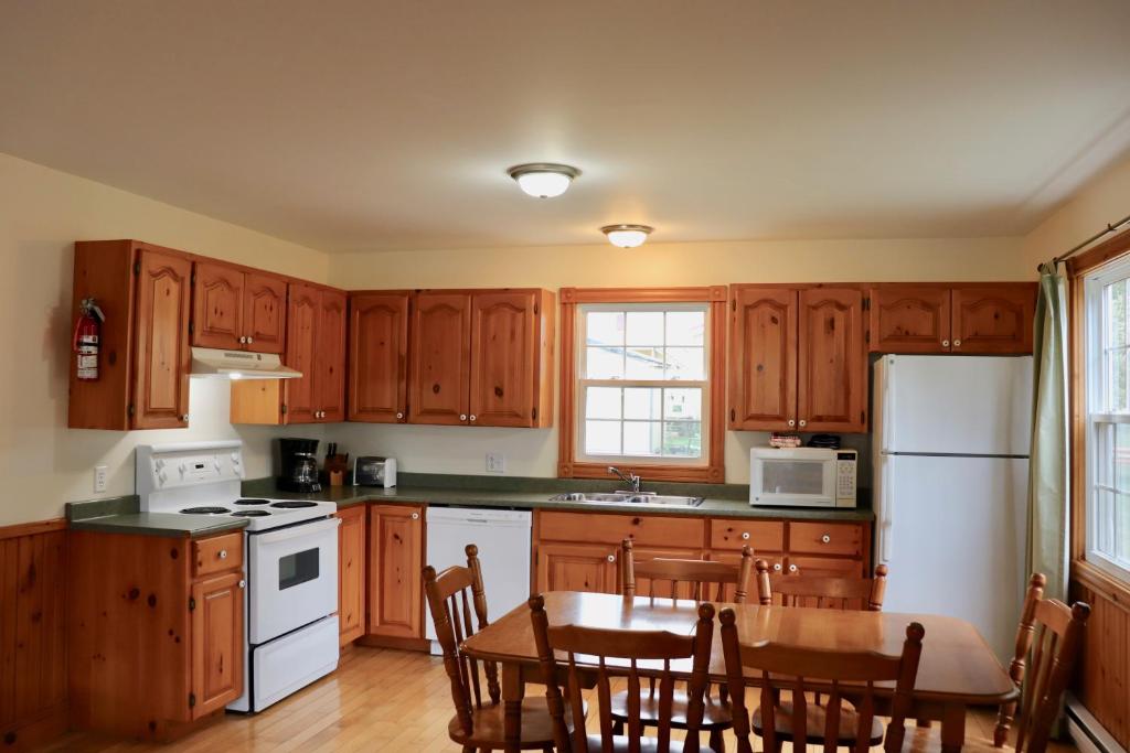a kitchen with wooden cabinets and a table and a refrigerator at Shining Waters - Ingleside Cottages in Cavendish