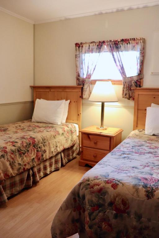 a bedroom with two beds and a lamp and a window at Shining Waters - Ingleside Cottages in Cavendish