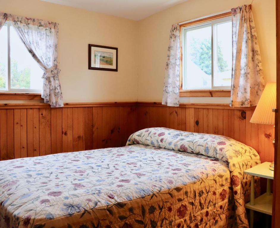 a bedroom with a bed and two windows at Shining Waters - Ingleside Cottages in Cavendish