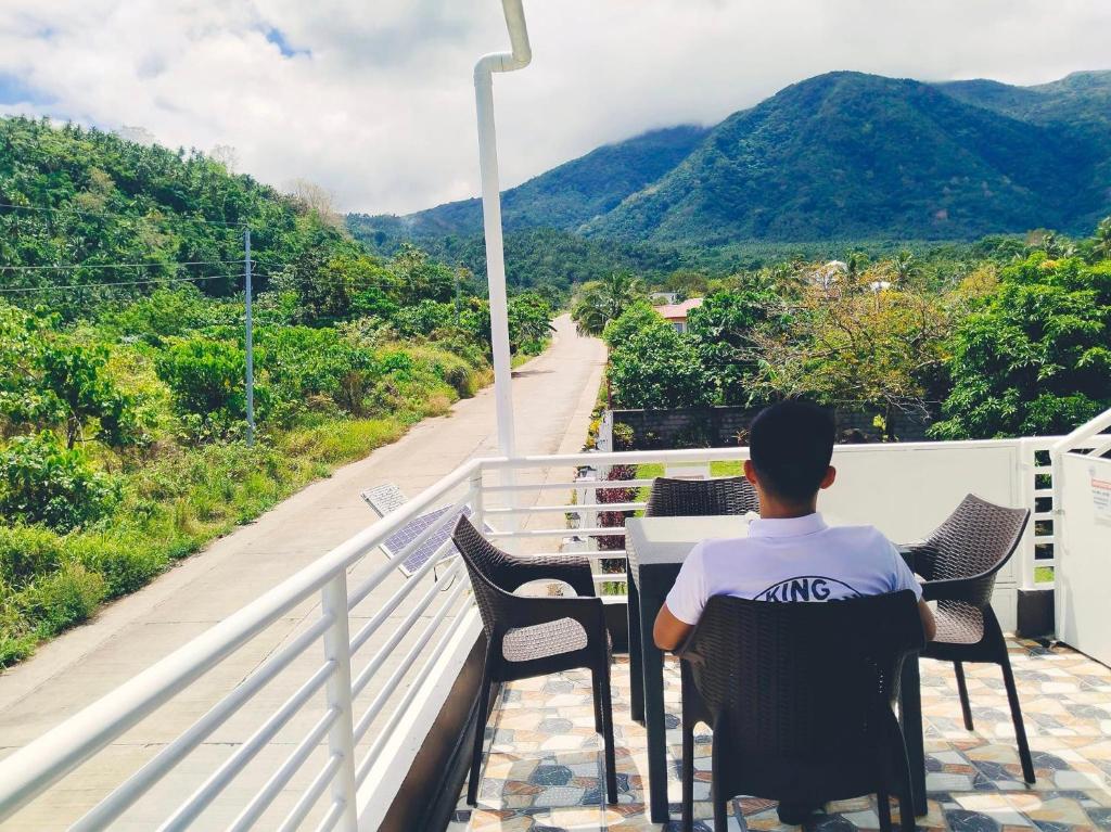 un homme assis à une table sur un balcon donnant sur une montagne dans l'établissement Kinghorn Garden House Resort, à Mambajao