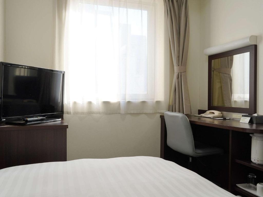 a hotel room with a bed and a desk with a television at Comfort Hotel Tokyo Kanda in Tokyo