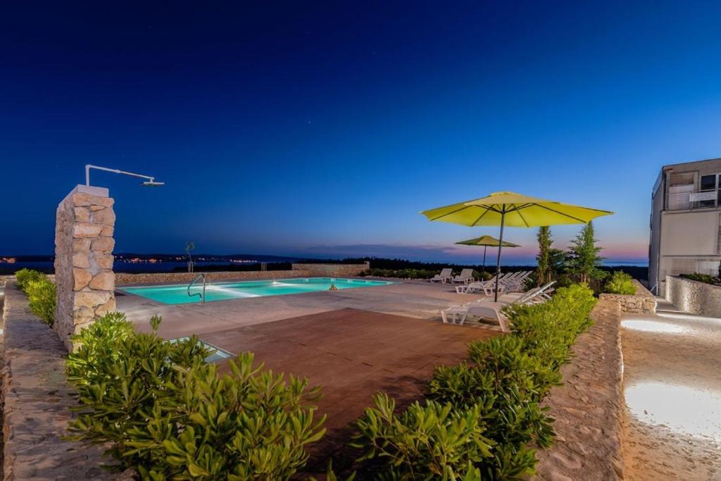 a swimming pool with a yellow umbrella and chairs and tables at Novaedil Apartment in Povljana