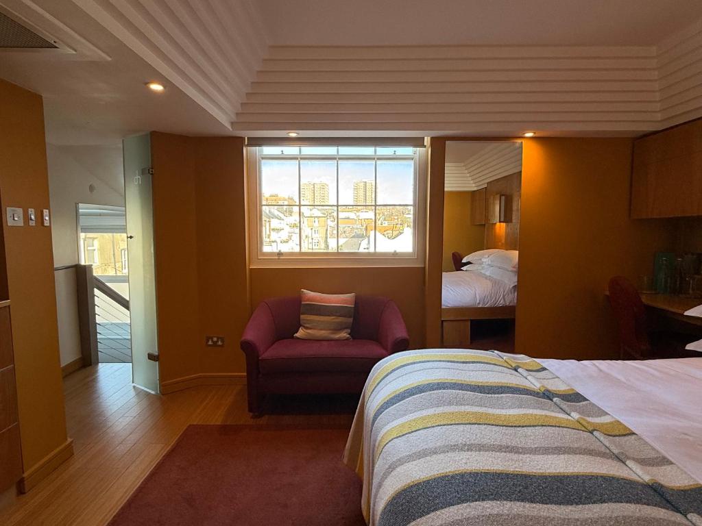 a bedroom with a bed and a chair and a window at Drakes Hotel in Brighton & Hove