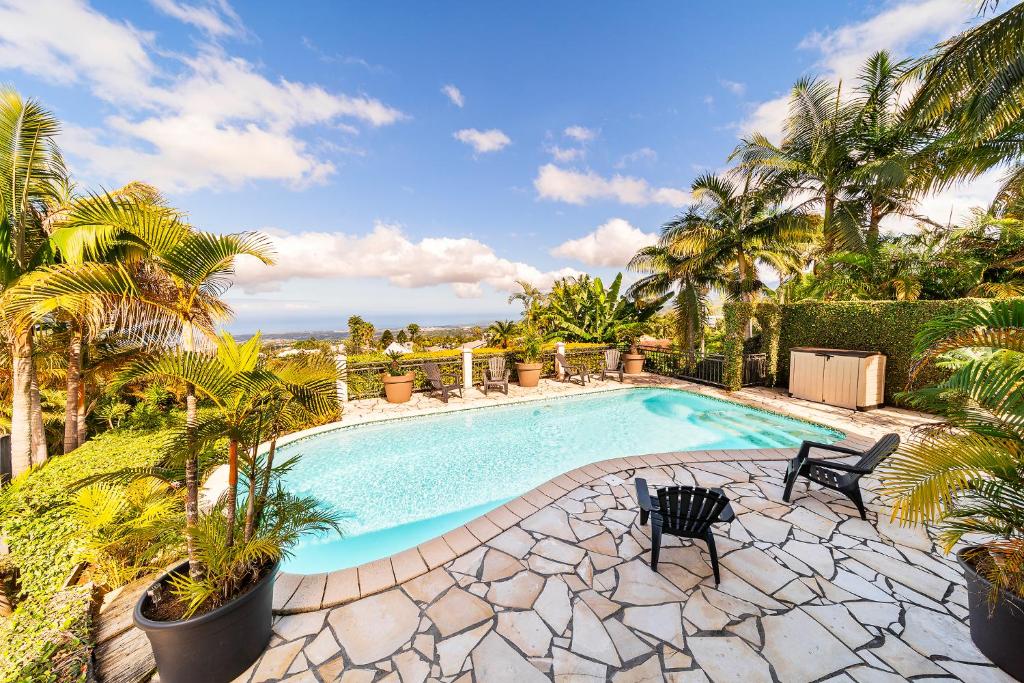 a swimming pool with palm trees and a resort at Villa Horizon Bleu - Vue Mer & Piscine Chauffée in Le Tampon