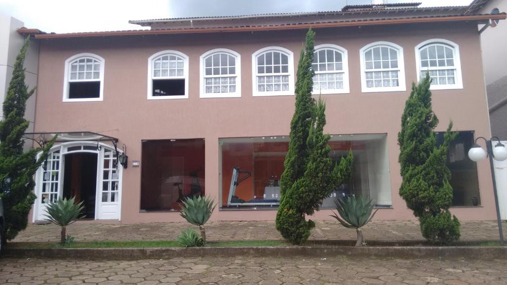 uma casa cor-de-rosa com árvores à frente. em Hotel Colonial Aquarius em João Monlevade