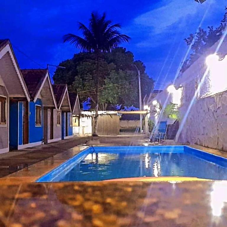 a pool at night with a palm tree in the background at Pousada do Sol in Pedra de Guaratiba