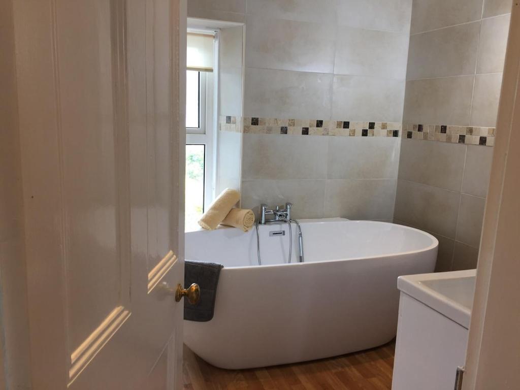 a white bath tub in a bathroom with a window at Sea Breeze Cottage on the North Wales Coast in Penrhyn Bay
