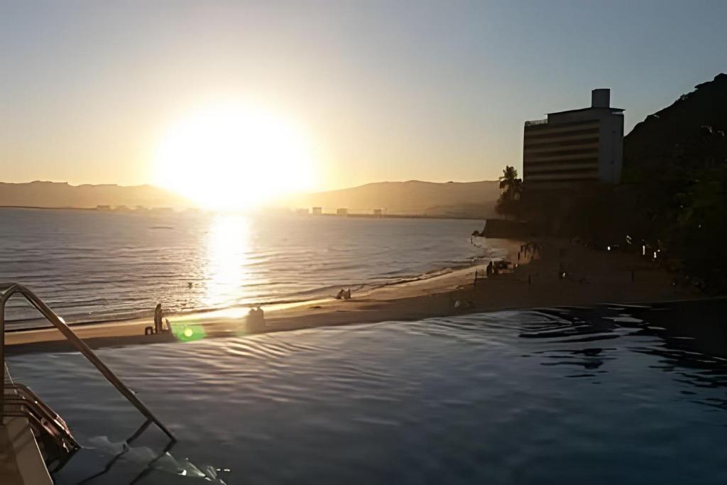 una piscina con playa y puesta de sol en Maravilhoso Apto Beira-Mar Prainha, Caraguatatuba com Piscina e Sauna, en Caraguatatuba