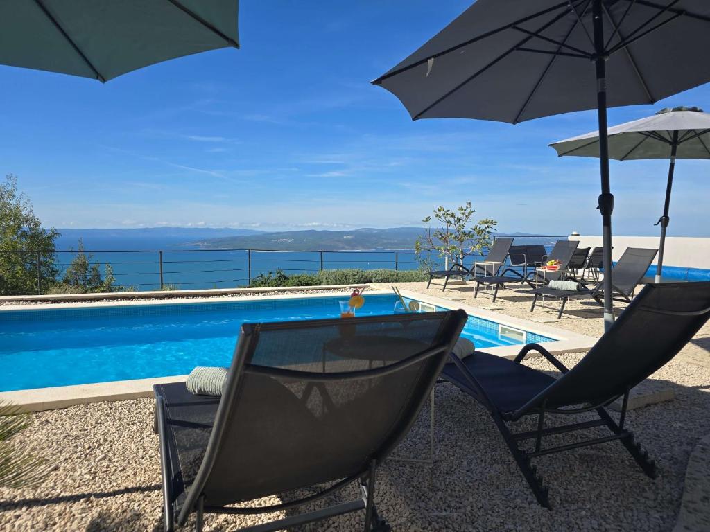Villa Alta Vista في Bast: زوج من الكراسي ومظلة بجانب مسبح