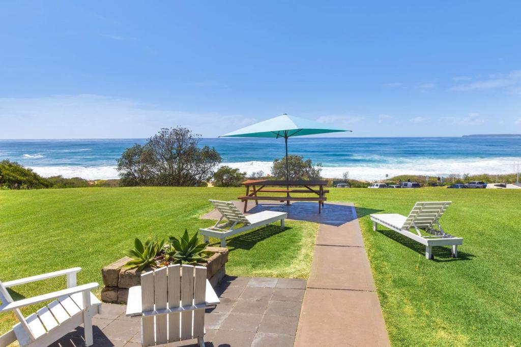 a picnic table and benches with the ocean in the background at Glory House at Culburra - Beachfront in Culburra Beach