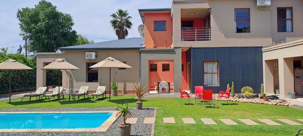 a house with a swimming pool and chairs and umbrellas at Karoo Sun Guest House in Oudtshoorn