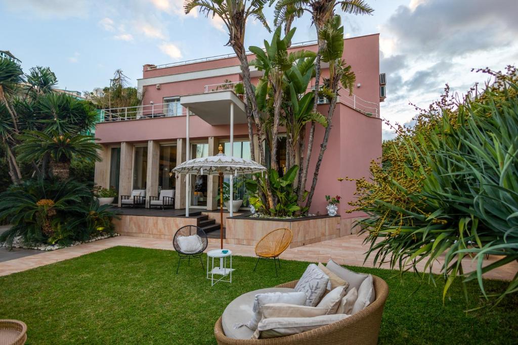 a pink house with a yard with chairs and an umbrella at Villa Olimpia in Mondello