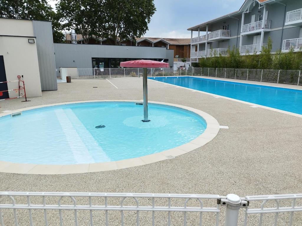 une petite piscine avec un parasol au milieu dans l'établissement Couleurs Pyla T3 grande terrasse Piscine commune, à La Teste-de-Buch