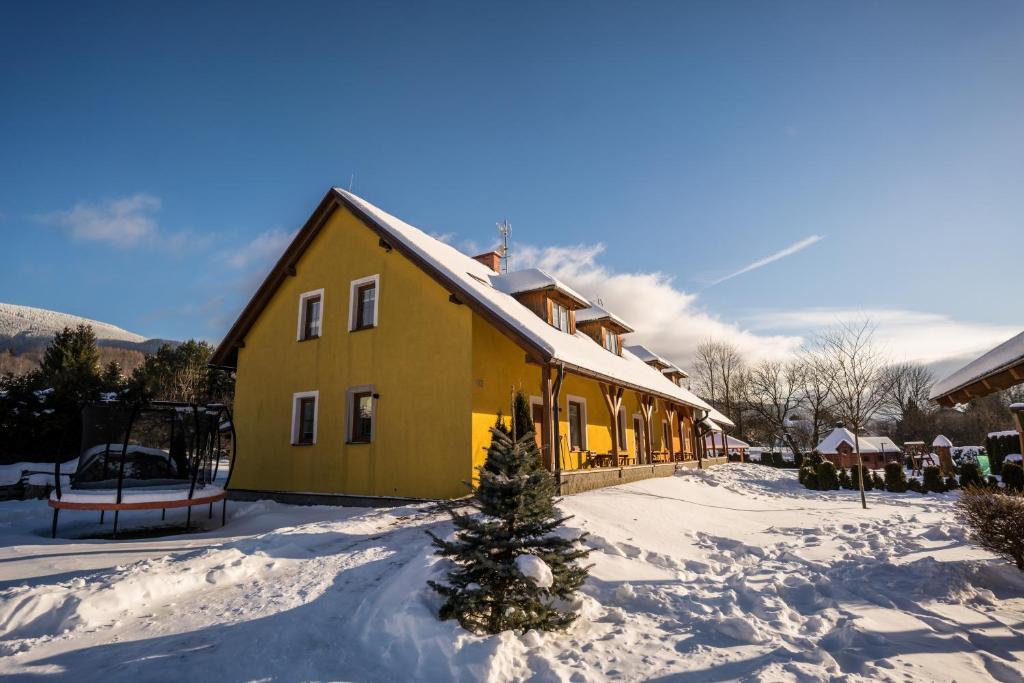 a yellow house with a christmas tree in the snow at Aparmány Loučná nad Desnou in Loučná nad Desnou