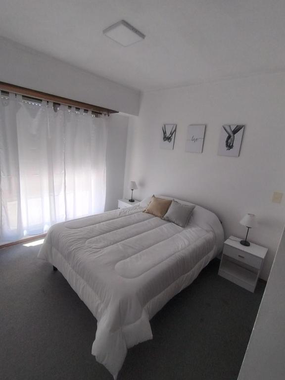 a white bedroom with a large bed and a window at Departamento 9 de Julio in Tandil
