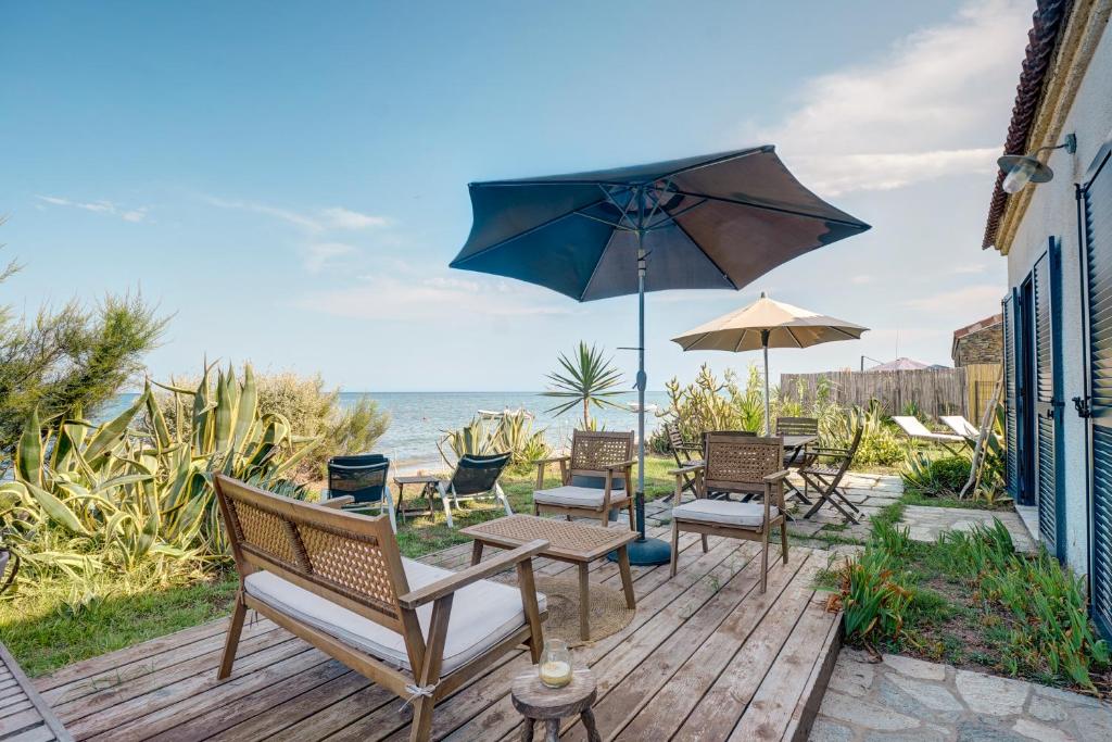 eine Terrasse mit Stühlen, einem Tisch und einem Sonnenschirm in der Unterkunft A Stalla - Maison pieds dans l'eau à Lucciana in Lucciana