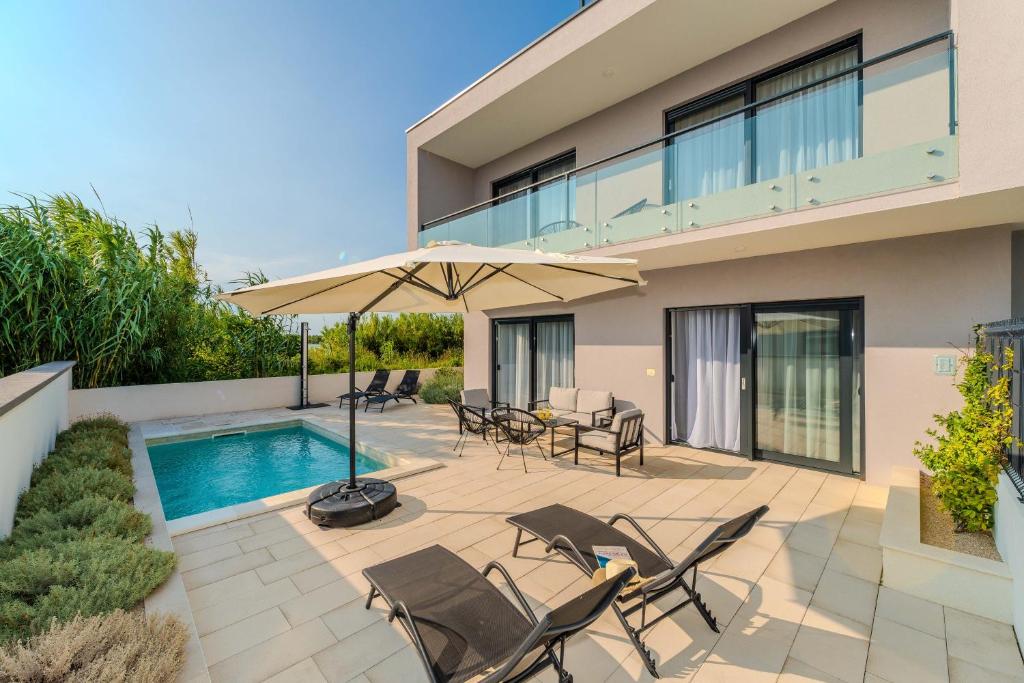 a patio with chairs and an umbrella next to a swimming pool at Beachfront Villa Jugo with Seaview in Privlaka