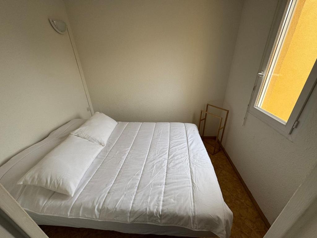 Cette petite chambre dispose d'un lit blanc et d'une fenêtre. dans l'établissement Appartement 4 personnes à 50 m de la plage, à Narbonne
